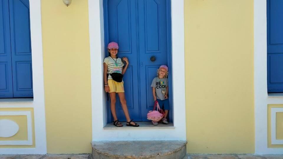 Ayla and Romy standing in front of a bright blue doorway on the gorgeous island of Meis in Greece, a short boat trip from Turkey