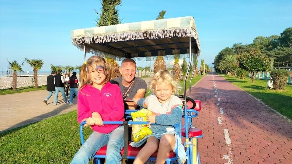 Ayla, Colin, and Romy in one of the family-sized bikes, riding along Batumi Boulevard on a sunny day