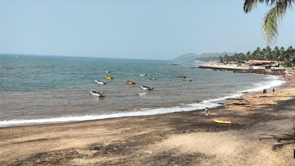 Black and golden sand and boats in the water at Anjuna beach in North Goa