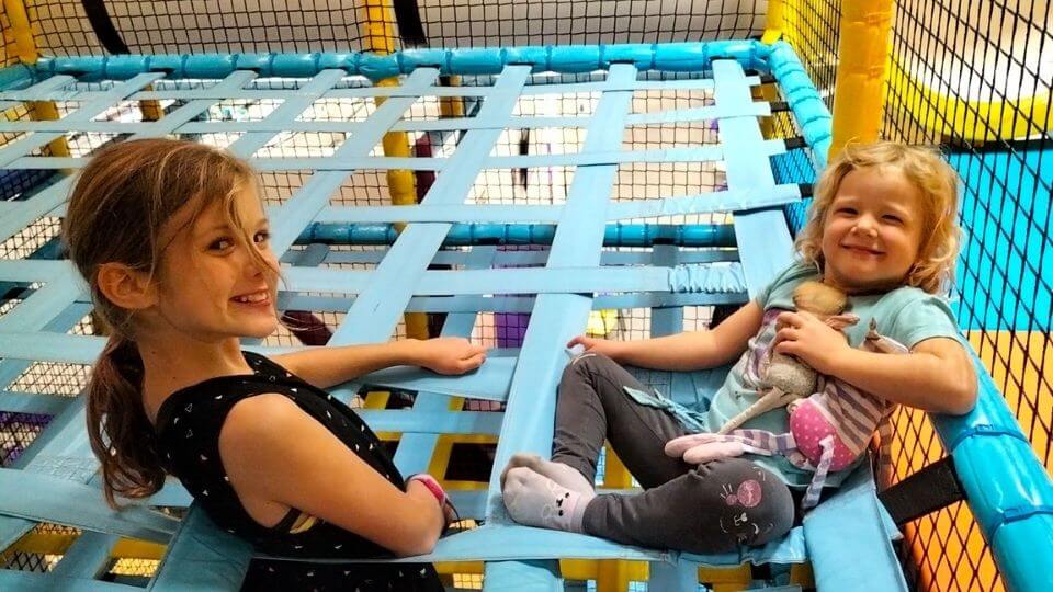 Ayla and Romy smile as they sit in the climbing lattice at Chipmunks Playland in Northland, Melbourne
