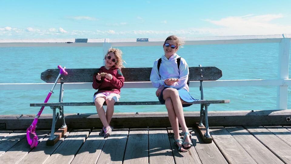 Romy and Ayla sitting on a bench on the Urangan Pier at Hervey Bay with the vast ocean behind them.