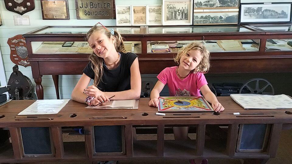 Ayla and Romy sit at an old school desk in the Childers Historic Complex.