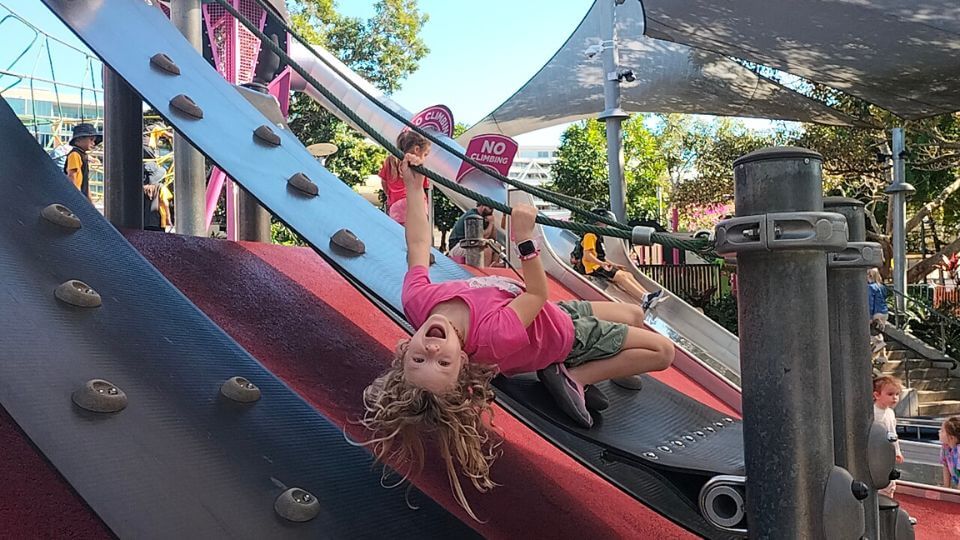 Romy hanging upside down and smiling at the Riverside Green Playground at Southbank.