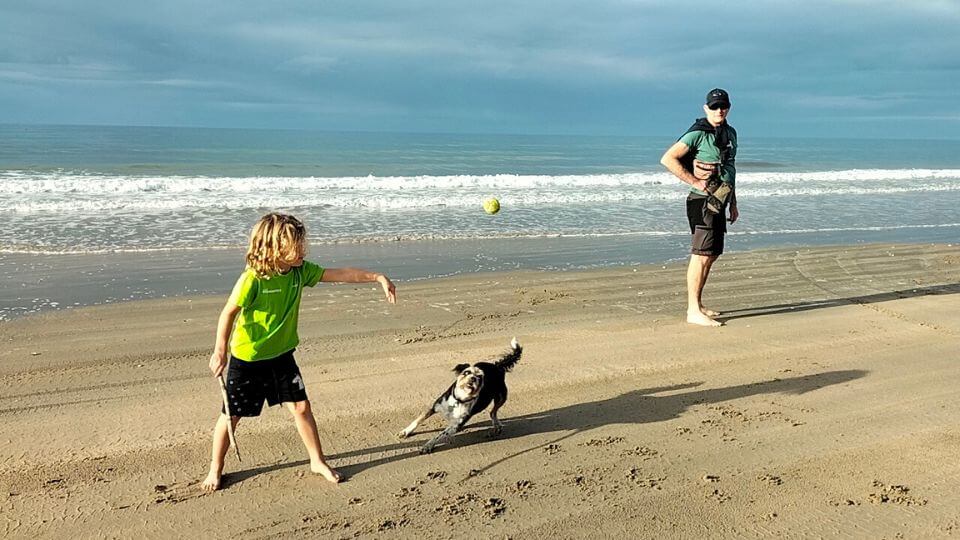 Romy throws a ball for Tui the dog with Colin in the background on Woodgate Beach in Queensland.