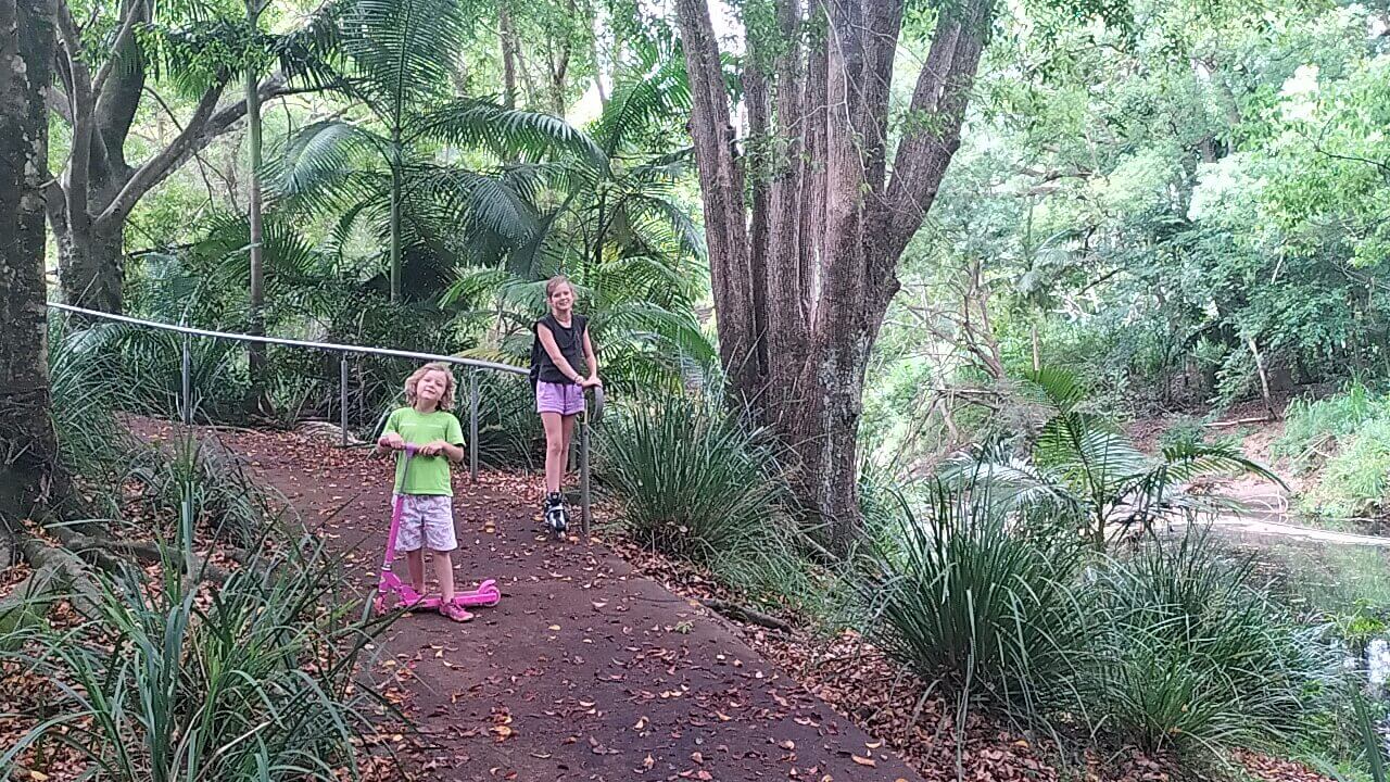 Ayla and Romy with their wheels, standing among the greenery of the Gary Evans walkway in Nambour.