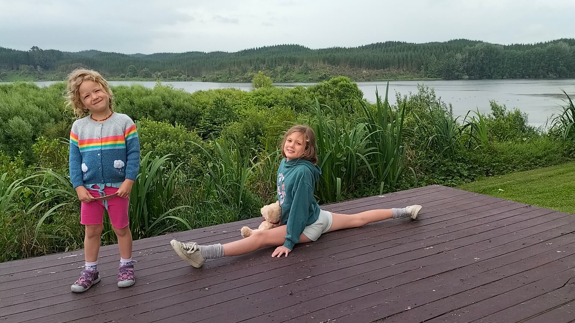 Ayla doing the splits with her sister and teddy bear in front of Lake Aniwhenua near Galatea, New Zealand.