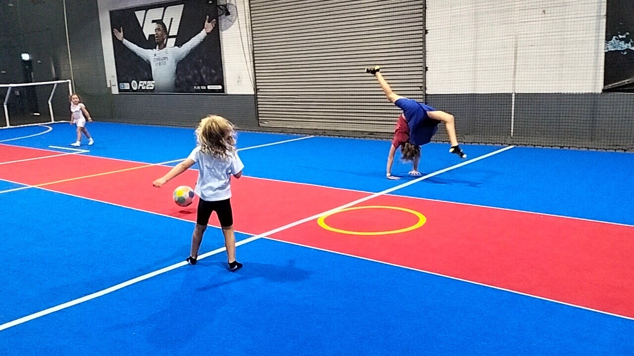Ayla practicing her gymnastics skills at an indoor play space in Cairns, while Romy kicks a ball.