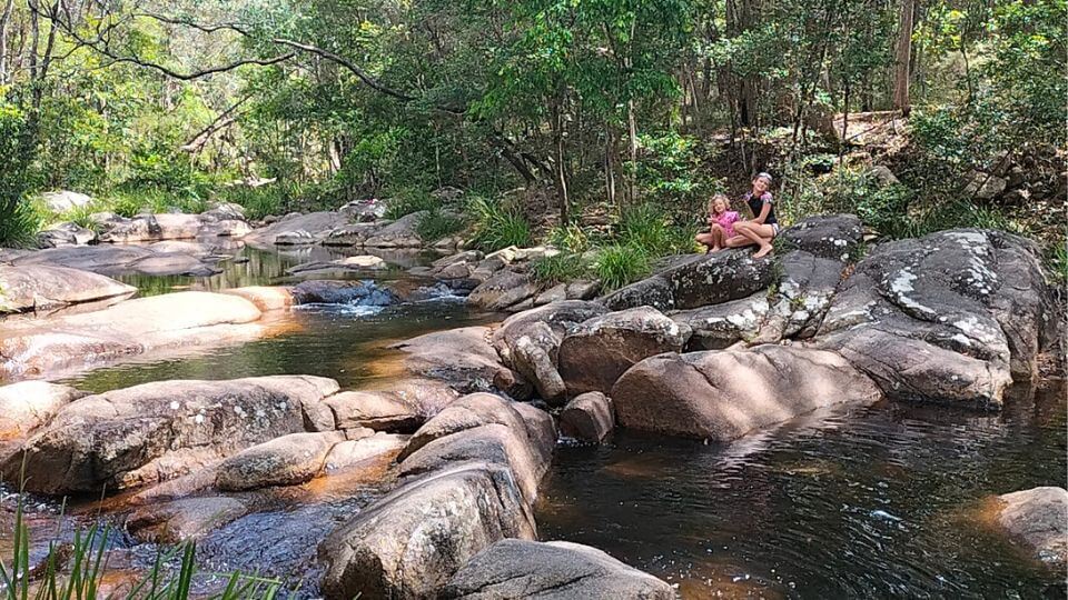 Ayla and Romy sit on a rock beside the stream at Mothar Mountain Rock Pools near Gympie.
