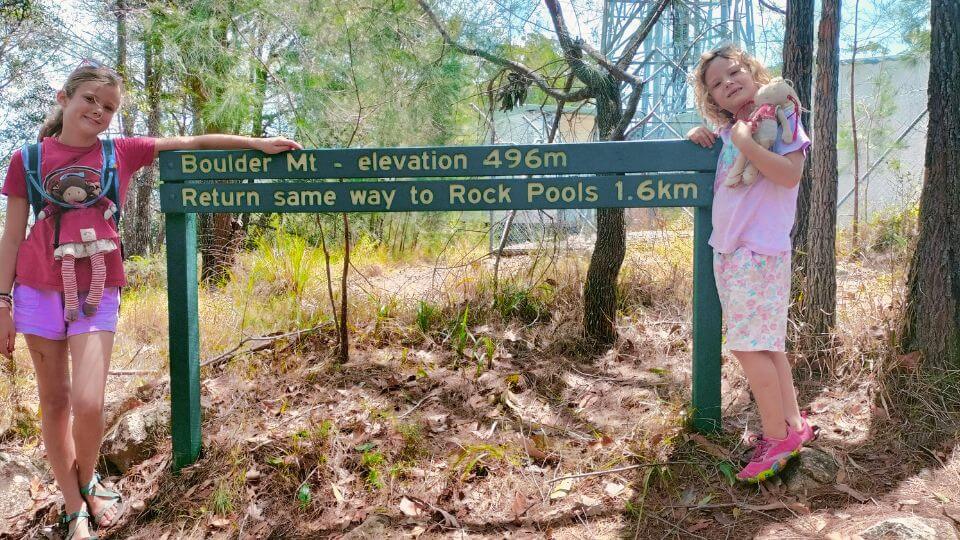Ayla and Romy stand next to the summit sign on Boulder Mountain, an excellent hike near Gympie.