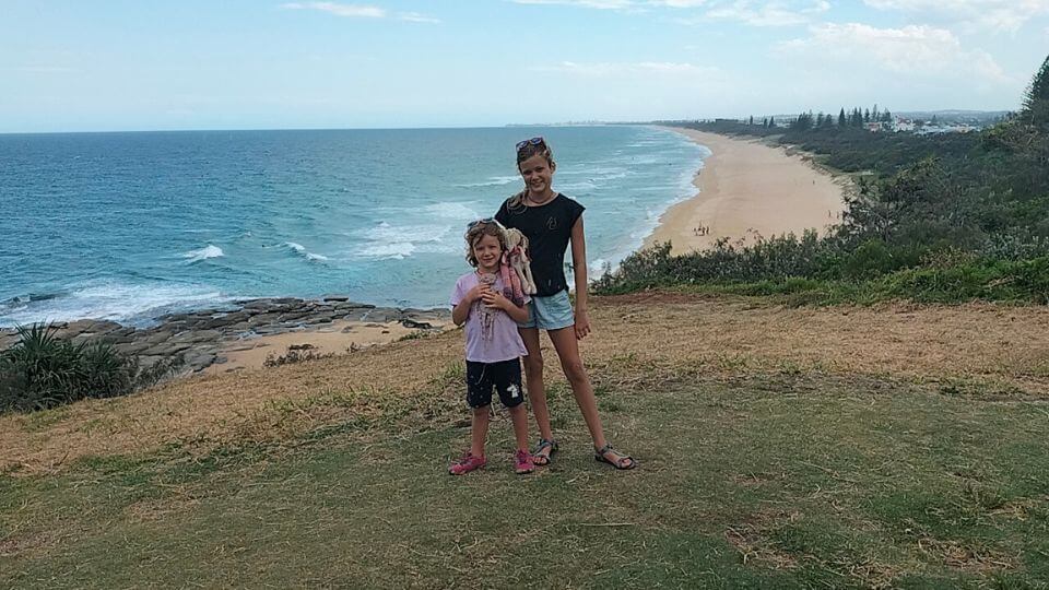 Ayla and Romy standing on the hillside at Point Cartwright Reserve in Mooloolaba on the Sunshine Coast, with a long stretch of beach down below.