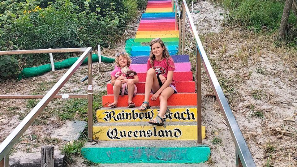 Romy and Ayla sit on the colorful steps at Rainbow Beach in Queensland.