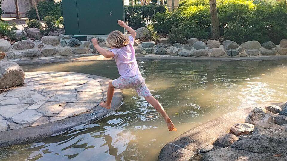 Romy jumps across a shallow stream at the Hinterland Adventure Playground in Cooroy.