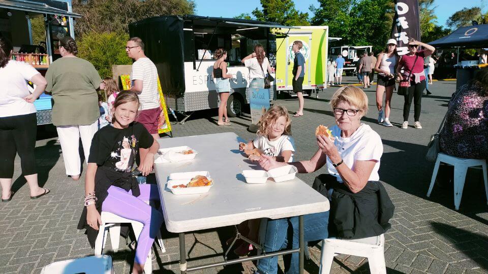 Ayla, Romy, and Nannie Annie enjoy dinner at the Rotorua Night Market on a sunny evening.