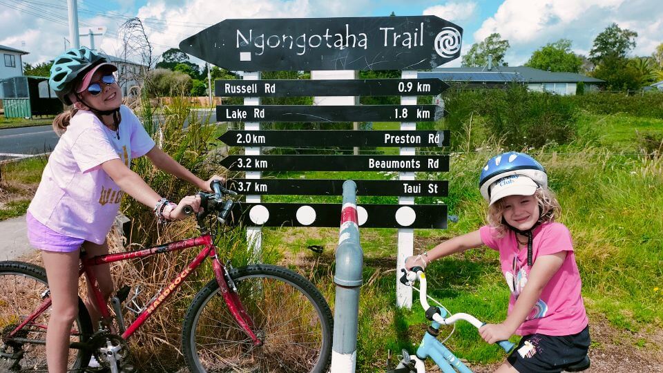 Ayla and Romy on their bikes in front of a sign for the Ngongotaha Trail.