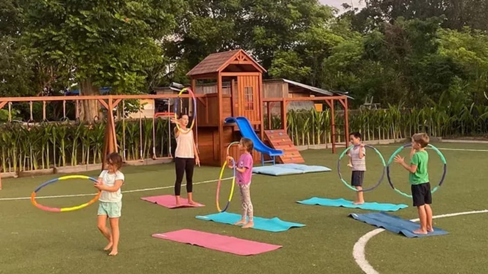 Kids and a fitness instructor doing a fun outdoor session with hoops and mats at a family wellness retreat at Pronoia Resort in Jimbaran Bay, Bali, Indonesia.