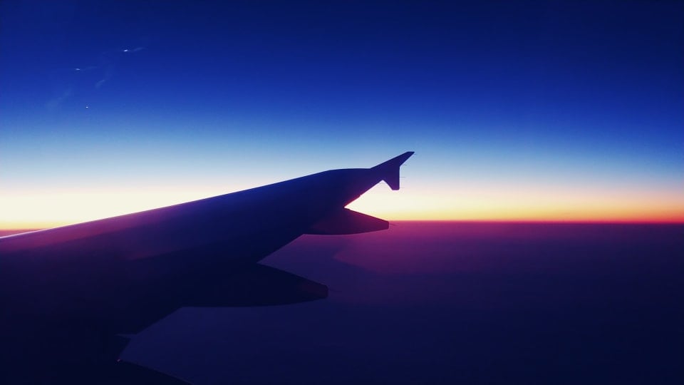A nighttime view out an airplane window with a sunset in the distance, and the sky appearing deep blue above.
