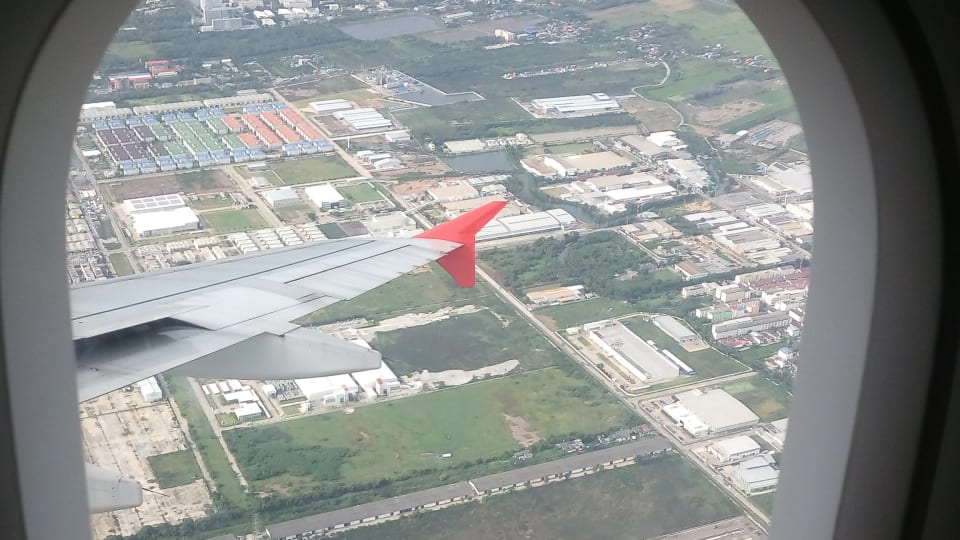 A view from a plane window of the plane's wing and buildings below.