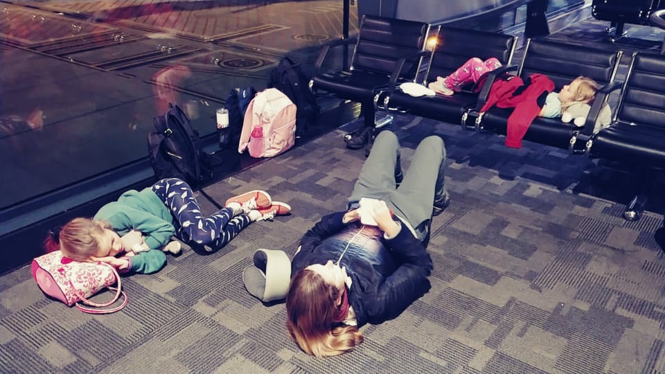 Ayla, Elly, and Romy try to get some rest on the floor and chairs at an airport late at night.
