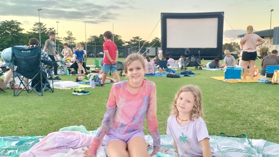 Ayla and Romy sitting on the grass at the Riverway Oval in Townsville, waiting for an outdoor movie to begin.