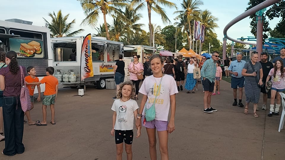 Ayla and Romy stand in front of food trucks at the Strand Night Markets in Townsville.