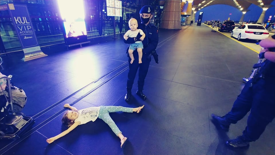Ayla lies on the ground outside Kuala Lumpur International Airport while a security guard holds Romy.