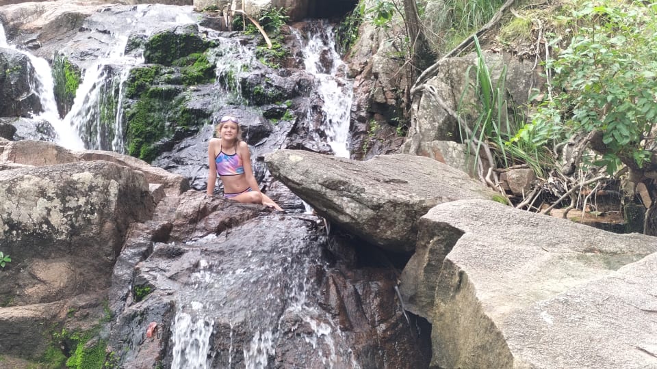 Ayla sits on a rock with picturesque waterfalls in the background at Endeavour Falls, Arcadia, Magnetic Island.