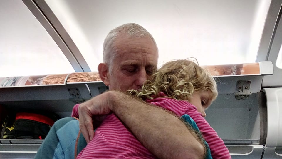 Colin carries Ayla in a cuddle on an airplane.