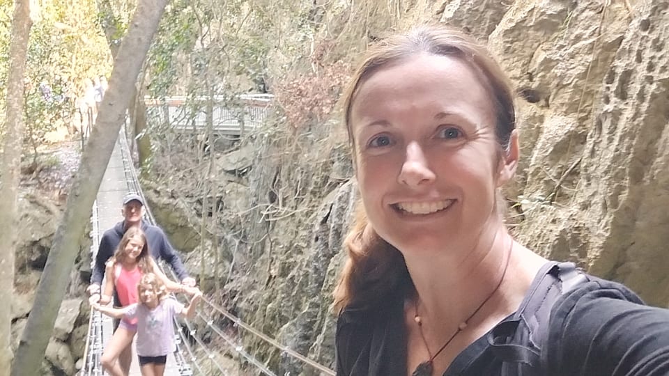 Elly takes a selfie, with Colin, Ayla, and Romy standing on a suspension bridge in the background at the Capricorn Caves near Rockhampton.