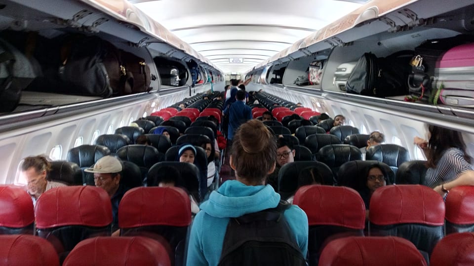 Elly walks down the aisle on an airplane, looking for her seat.