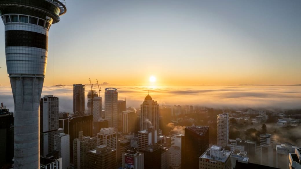 A captivating scene of Auckland’s skyline featuring the Sky Tower at dusk, illuminated against a backdrop of vibrant city lights and a clear evening sky.