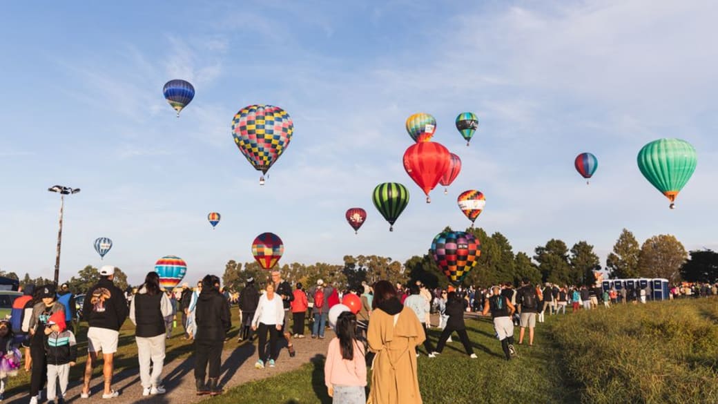 A vibrant hot air balloon festival in Hamilton, New Zealand with colorful balloons and a lively crowd.
