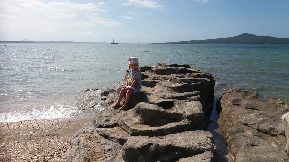 Ayla sits on a rock at St Heliers Beach in Auckland.
