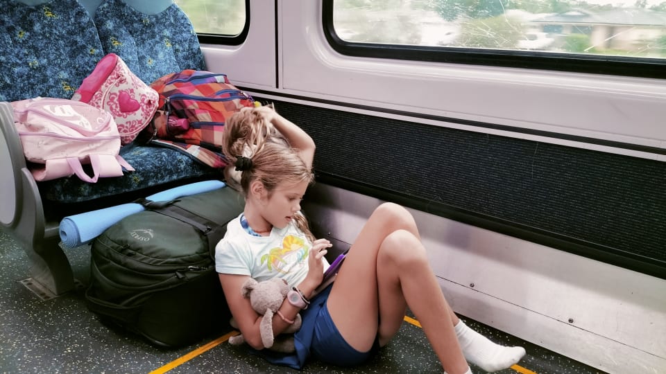 Ayla sits on the floor with all the luggage and reads her Kindle during a train trip in Australia.