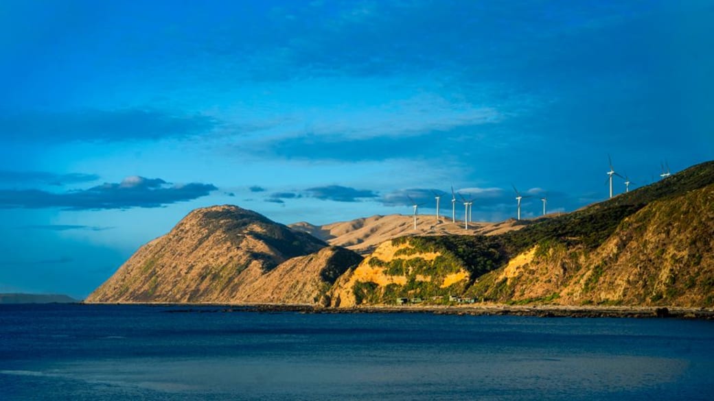 Stunning panorama of Wellington’s coastline featuring rolling hills, wind turbines, and a brilliant blue sky.