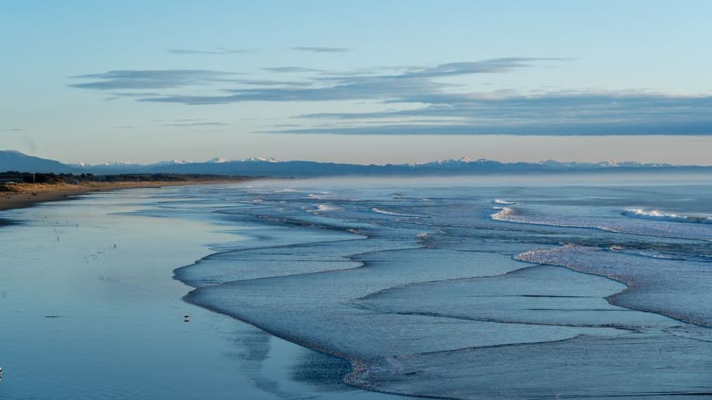 A panoramic shot of Christchurch’s shoreline, highlighting gentle surf and tranquil ocean beneath an expansive sky.