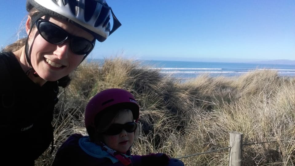 Elly and Ayla ride the biking trails at Bottle Lake Forest in Christchurch, with a view of the sea beyond.