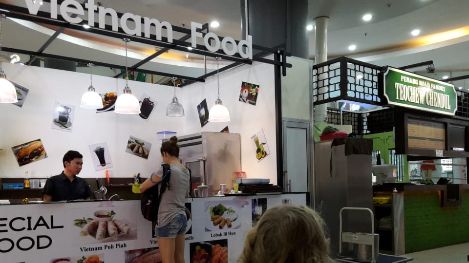 Elly gets food from a Vietnam Food stall while Ayla waits at the table.
