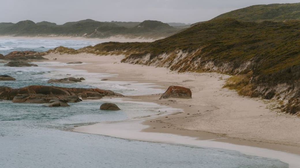 Peaceful view of Yallingup Beach with rolling waves, rocky shore, and misty hills in Western Australia.