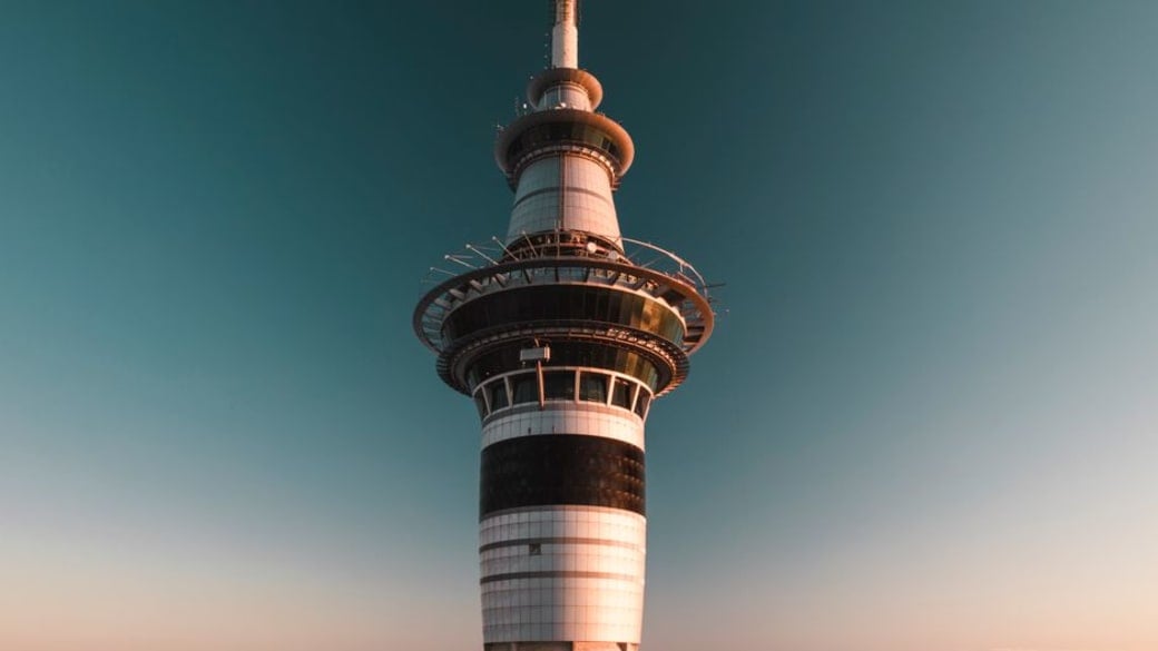 A photograph of the Sky Tower in Auckland, New Zealand, silhouetted against a vibrant sunset sky.