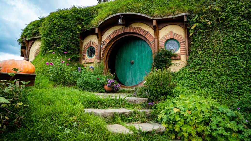 Picturesque Hobbiton house with a lush green roof and round door surrounded by vibrant garden.