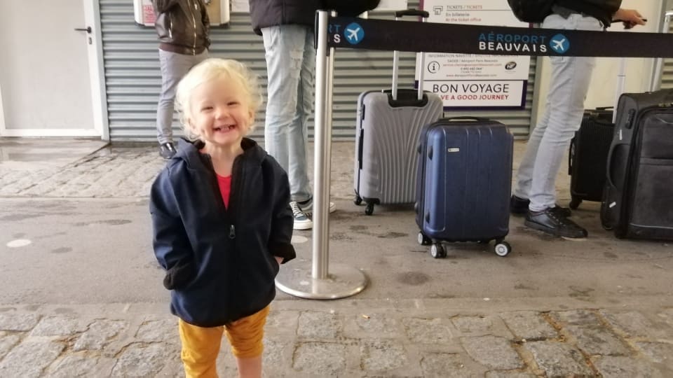 Romy smiles large with her hands in her jacket pockets during a family travel day in Europe.