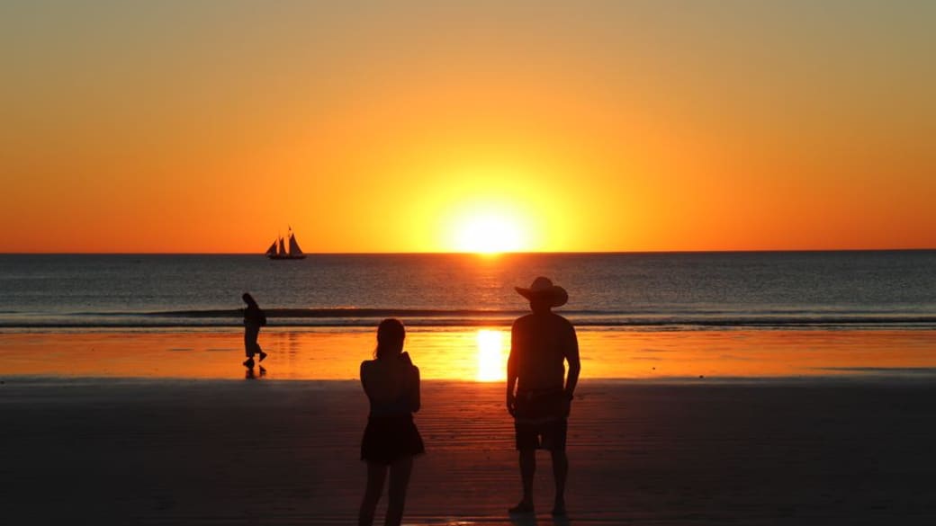 Silhouettes against a vibrant sunset at Cable Beach, Australia with a sailboat in view.