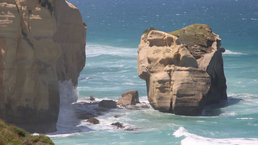 Stunning rocky coastal formations with waves crashing against them on a sunny day.