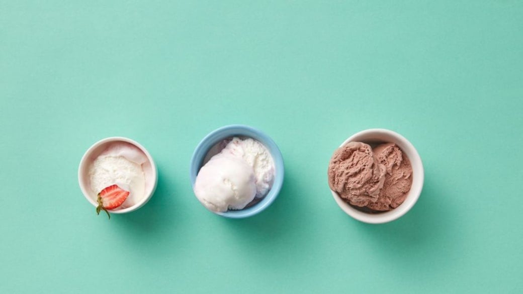Three different ice cream flavors in cups on a mint green background.
