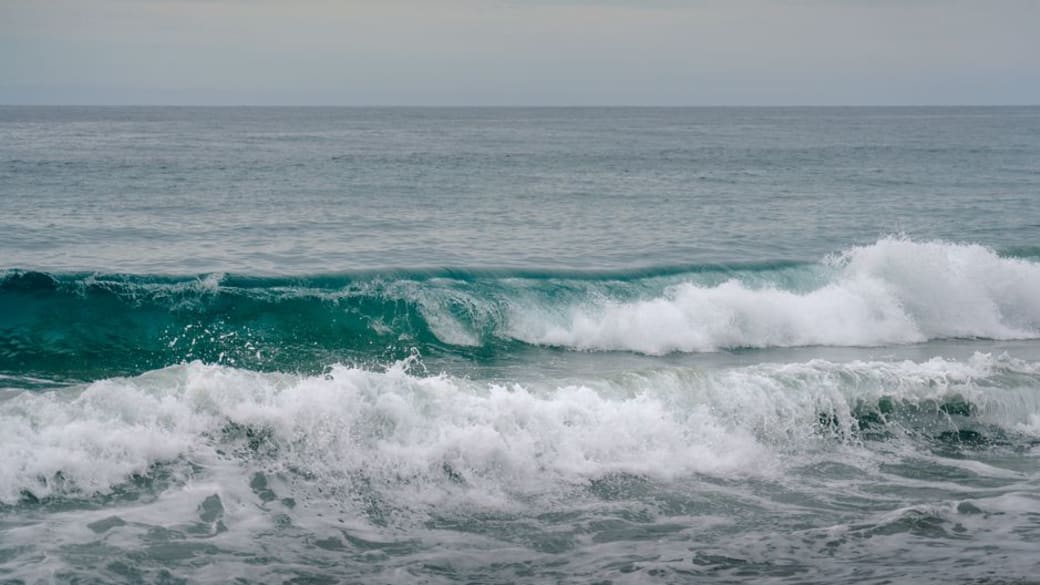 Tranquil view of ocean waves crashing onto the sandy shore under a calm cloudy sky.
