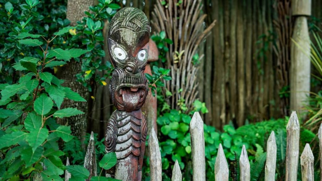 A traditional Maori carving surrounded by lush greenery in a New Zealand garden, showcasing cultural heritage.