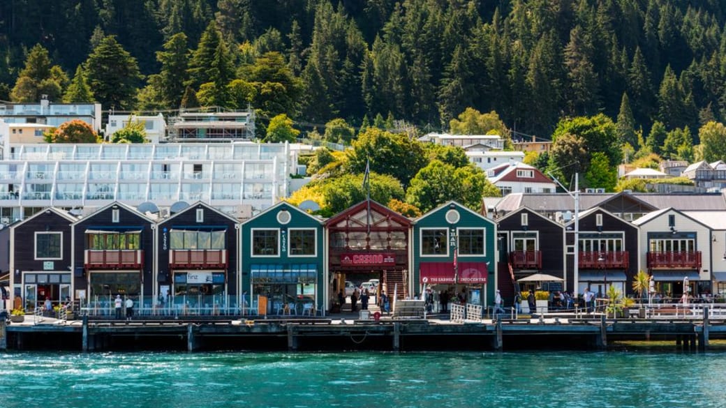 Colorful waterfront buildings in Queenstown with mountainous backdrop and vibrant greenery.