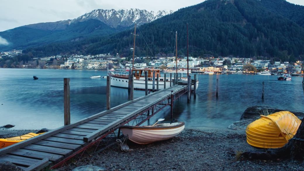 Picturesque view of Queenstown harbor with boats, dock, and mountains.