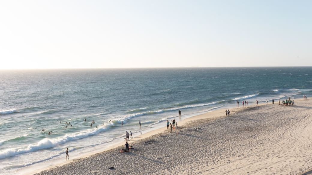 Tranquil aerial view of Cottesloe Beach in Perth with people enjoying the sunny seashore and crashing waves.
