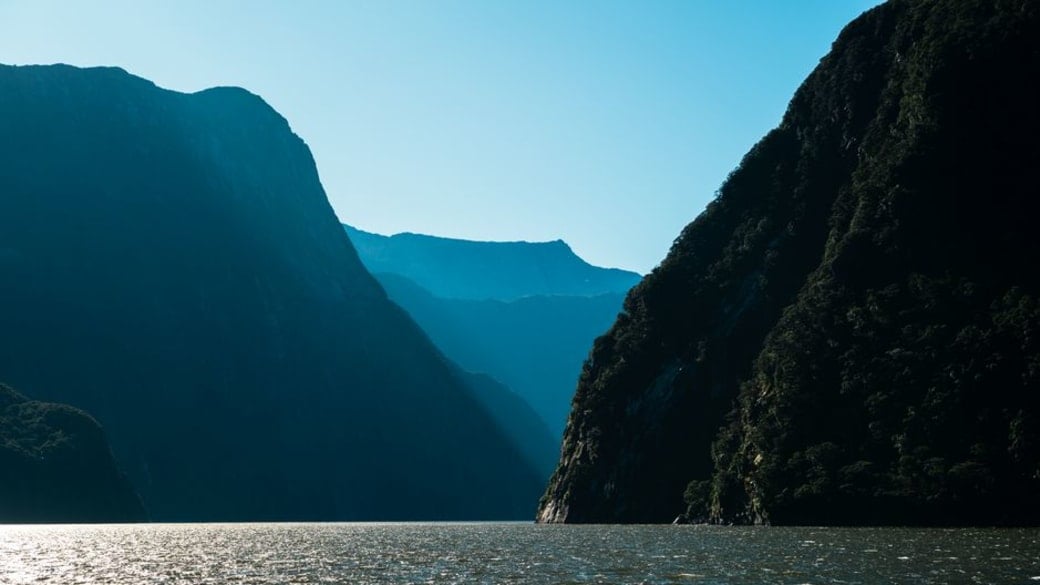 Tranquil view of Milford Sound's fjords and mountains under clear skies, New Zealand.